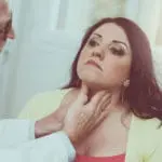 Doctor doing thyroid exam on female patient